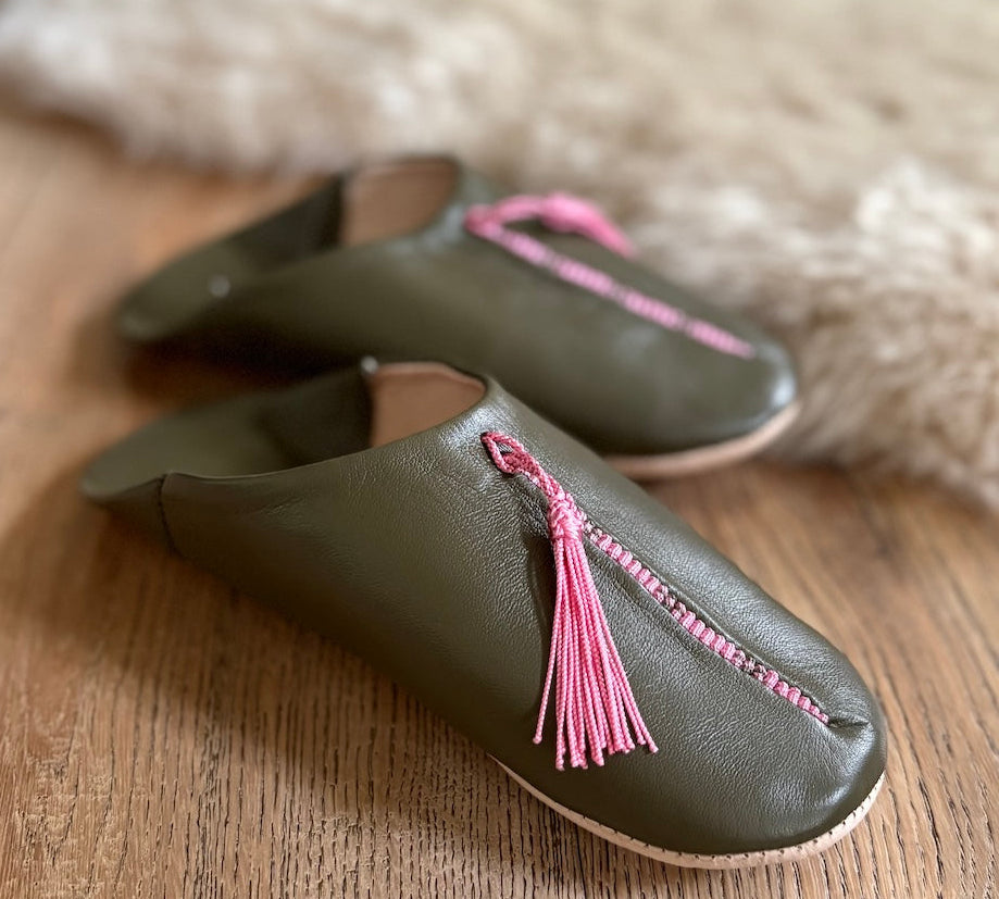 Pair of green leather slippers with pink tassels on a wooden surface.
