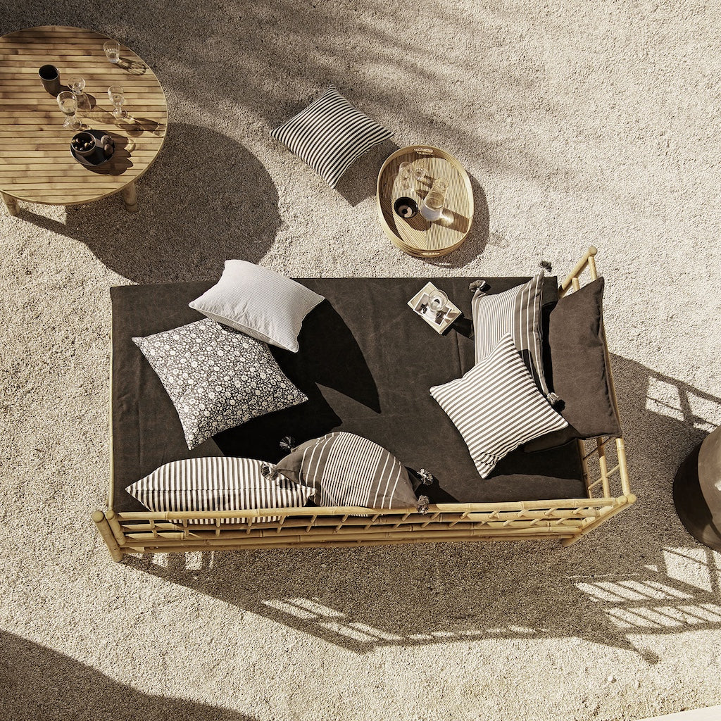 Outdoor seating area with a woven bench and cushions on a sandy surface.