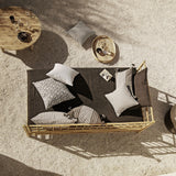 Outdoor seating area with a woven bench and cushions on a sandy surface.