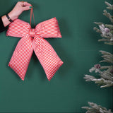 Red and white striped bow held by a hand on a green background with a disco ball and Christmas tree.