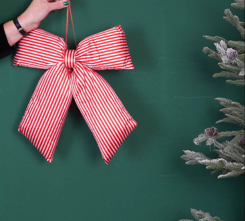 Red and white striped bow held by a hand on a green background with a disco ball and Christmas tree.
