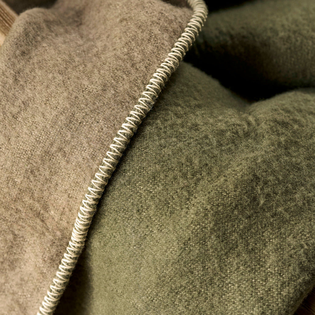 Close-up of a soft woven textile in muted olive green with a contrasting beige braided trim running along the edge.