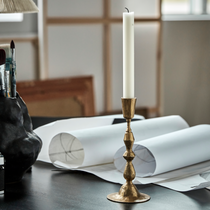 Gold candlestick with a white candle on a table with art supplies and papers.