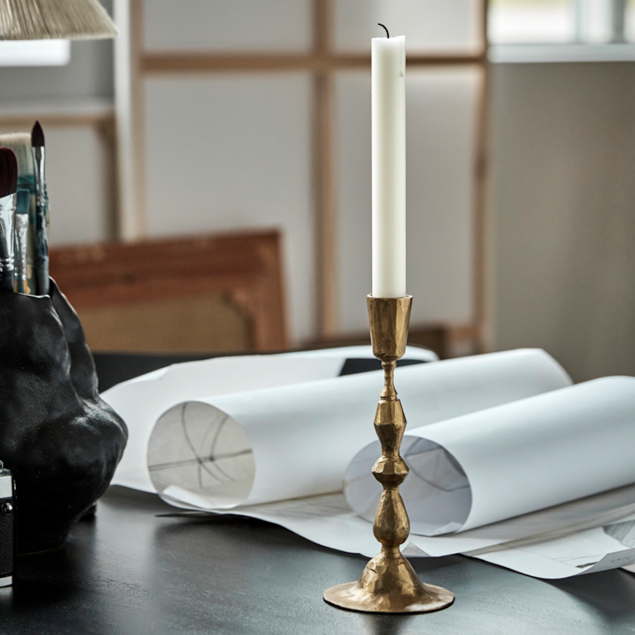 Gold candlestick with a white candle on a table with art supplies and papers.