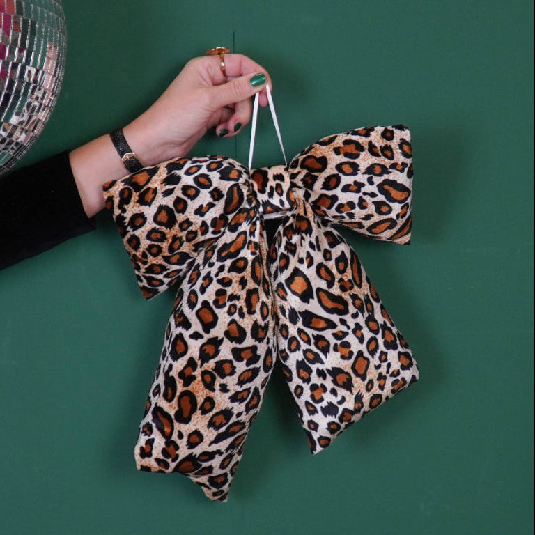 Hand holding a leopard print bow with a disco ball and Christmas tree on a green background
