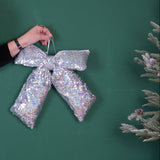 Hand holding a silver sequin bow with a disco ball and Christmas tree on a green background