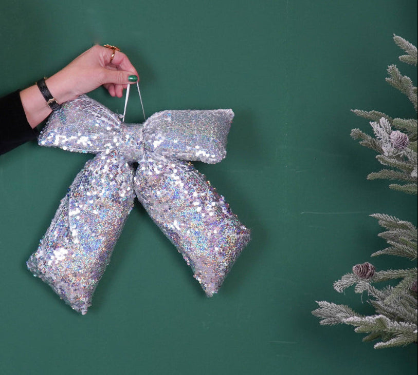 Hand holding a silver sequin bow with a disco ball and Christmas tree on a green background