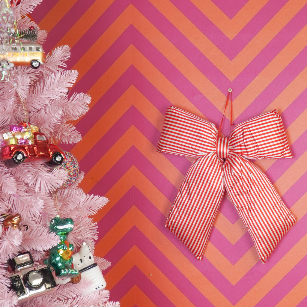 Decorative red and white striped bow on a pink and orange chevron wall with a pink Christmas tree.