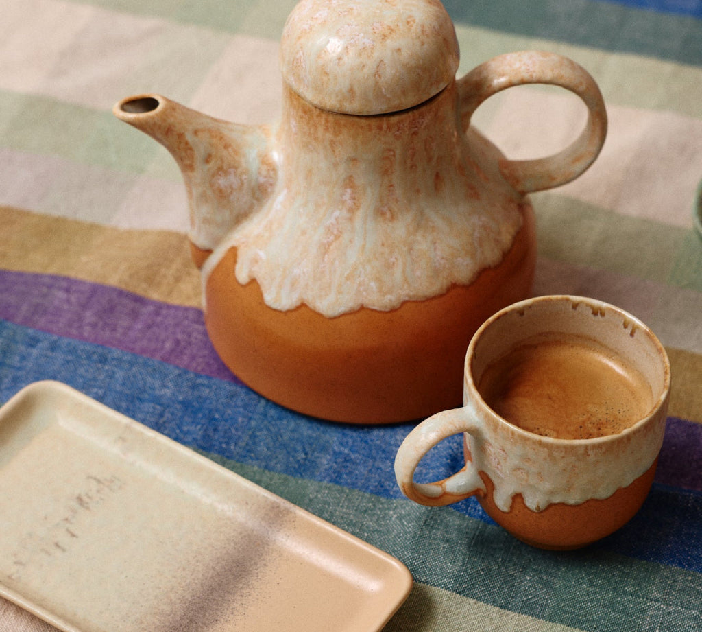 Ceramic teapot and mug on a colorful striped tablecloth