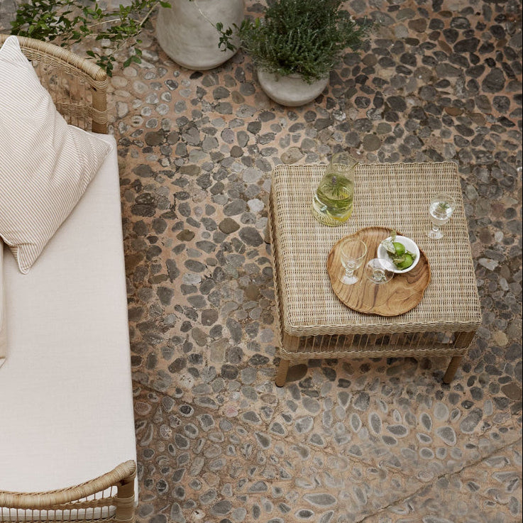 Rattan sofa with cushions and a small table on a stone patio