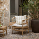 rattan chair with white cushion in an outdoor setting with stone wall and plant.