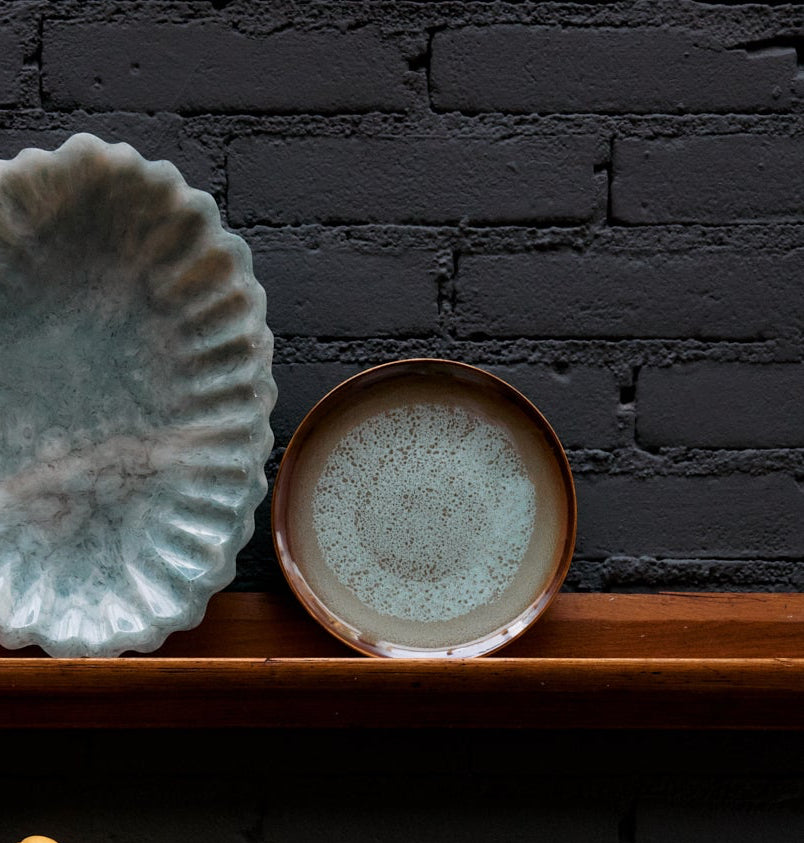 Three ceramic plates on a wooden shelf against a black brick wall.