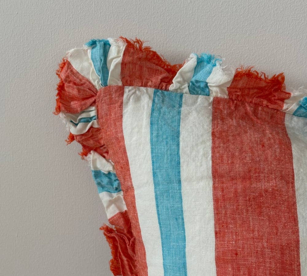 Close-up of coral stripe linen cushion fringe ruffle edge detail showing raw linen fraying in coral, aqua and white