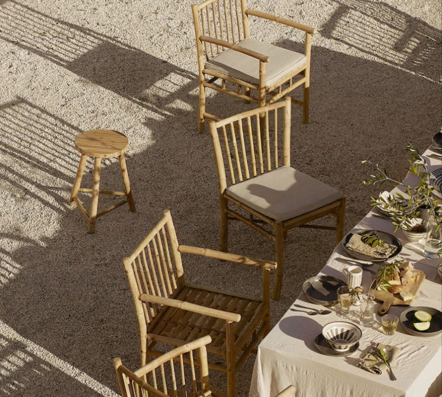 A set of bamboo dining chairs with cushions, placed outdoors around a dining table.