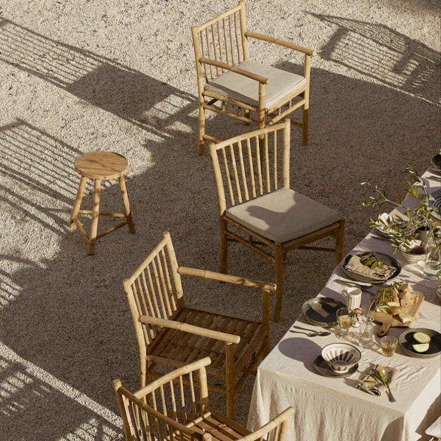 A set of bamboo dining chairs with cushions, placed outdoors around a dining table.