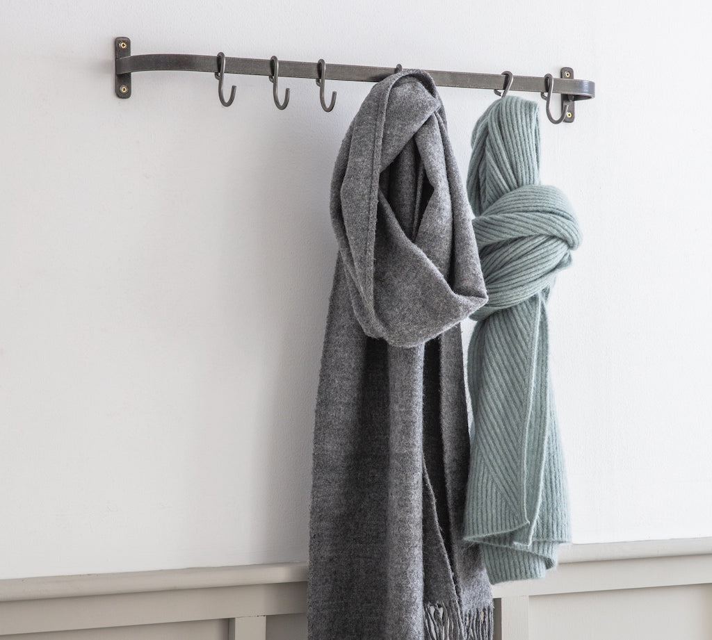 Two scarves hanging on a metal rack against a white wall.