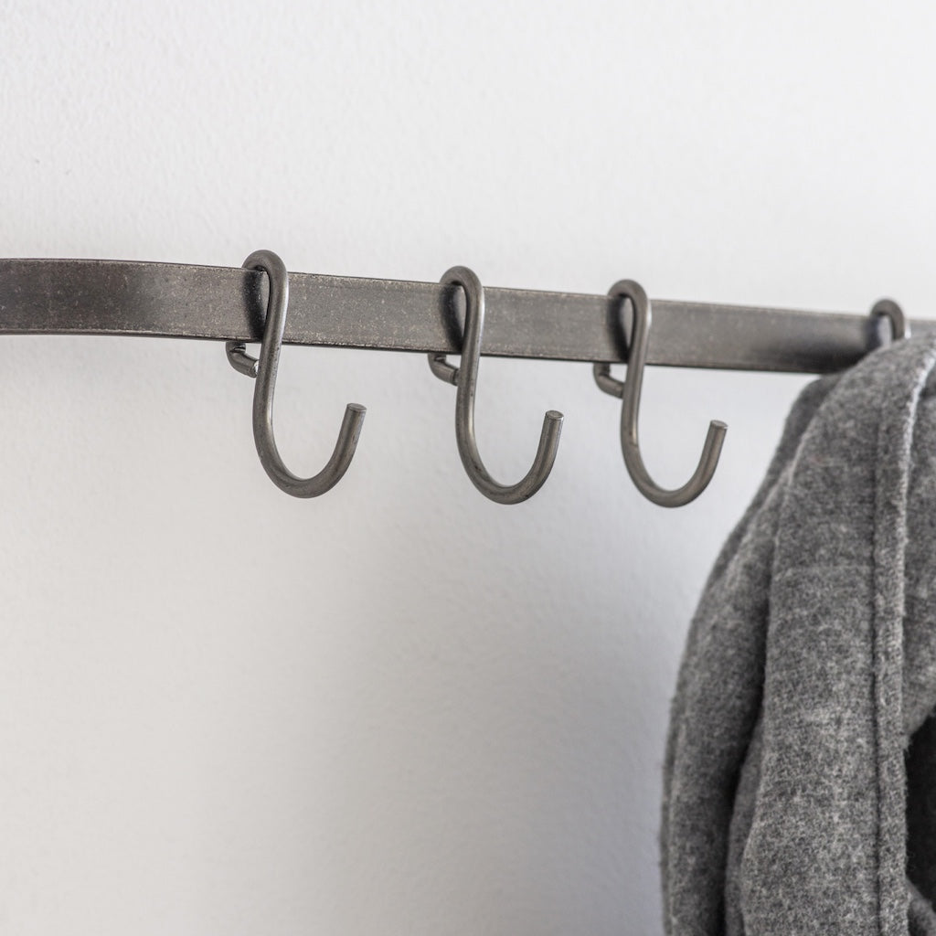Metal coat rack with hooks against a white wall, featuring a gray coat.