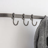Metal coat rack with hooks against a white wall, featuring a gray coat.