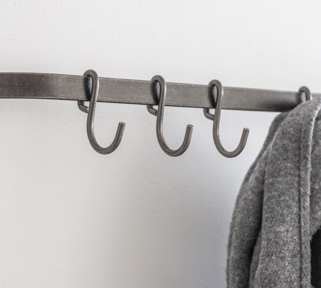 Metal coat rack with hooks against a white wall, featuring a gray coat.