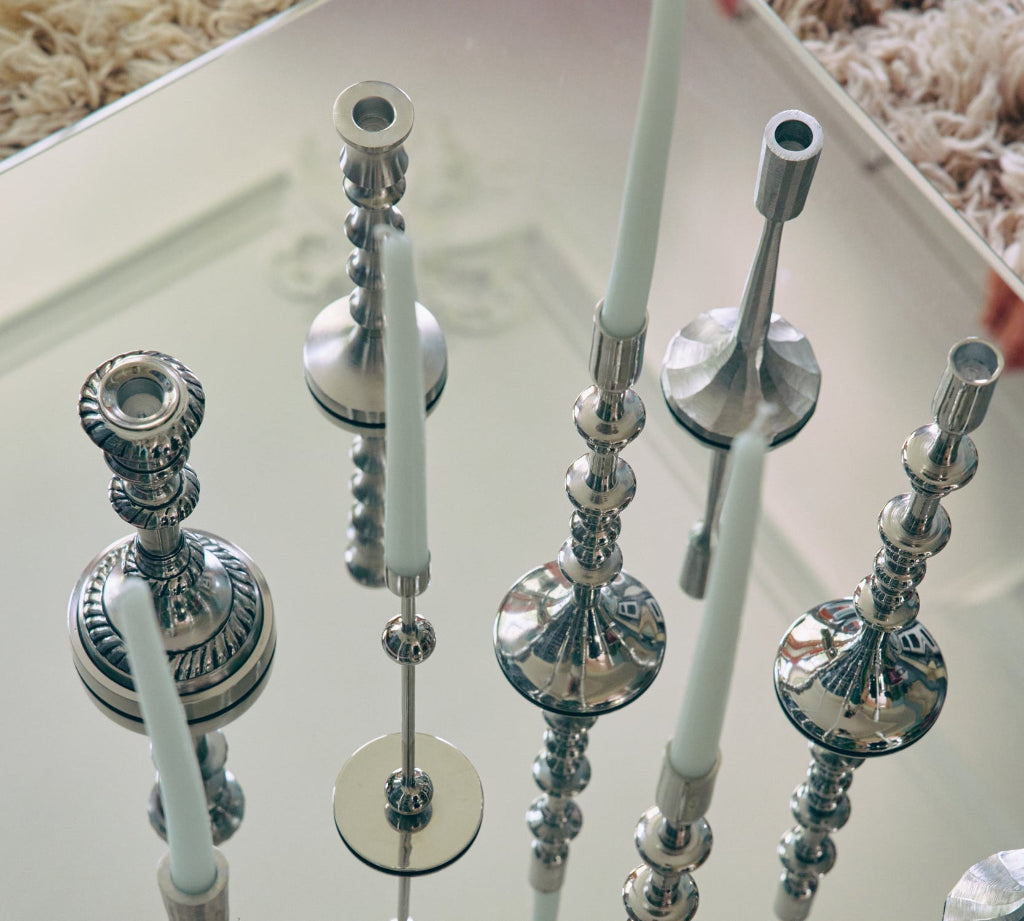 Silver candle holders with white candles on a reflective surface