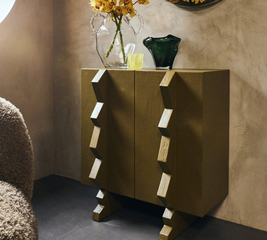 Modern interior with an olive green side table, round mirror, and yellow flowers.