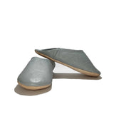 A pair of slip-on mule slippers in a dusty blue-gray color with a natural tan sole, displayed on a clean white background.