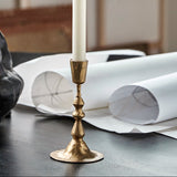 Gold candlestick with a white candle on a table with art supplies and papers.