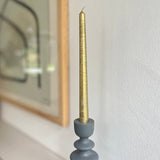 Gold candle in a gray holder against a white wall with a blurred mirror in the background