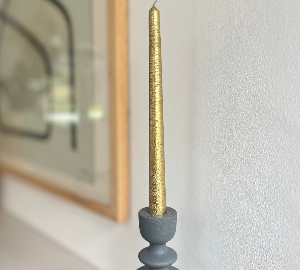 Gold candle in a gray holder against a white wall with a blurred mirror in the background