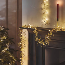Decorative lights on a fireplace mantel with a Christmas tree and candle.