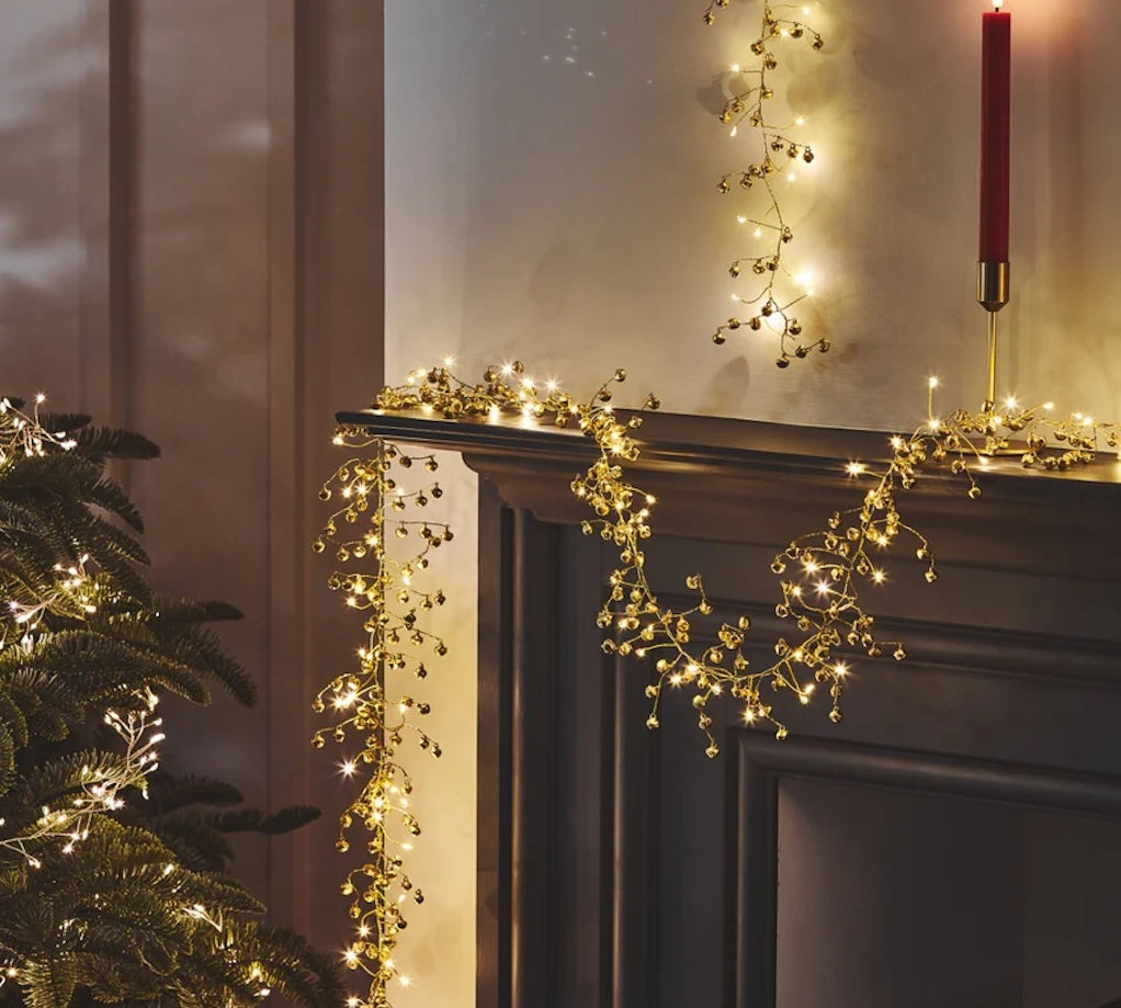 Decorative lights on a fireplace mantel with a Christmas tree and candle.