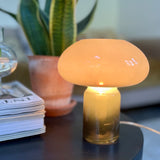 Green mushroom-shaped lamp on a table with a plant and magazine in the background