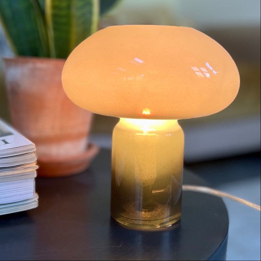 Green mushroom-shaped lamp on a table with a plant and magazine in the background