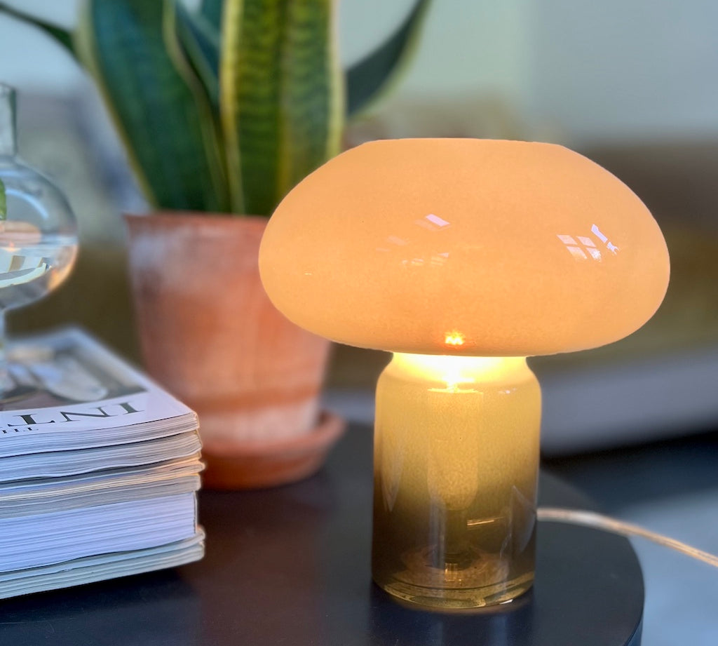 Green mushroom-shaped lamp on a table with a plant and magazine in the background