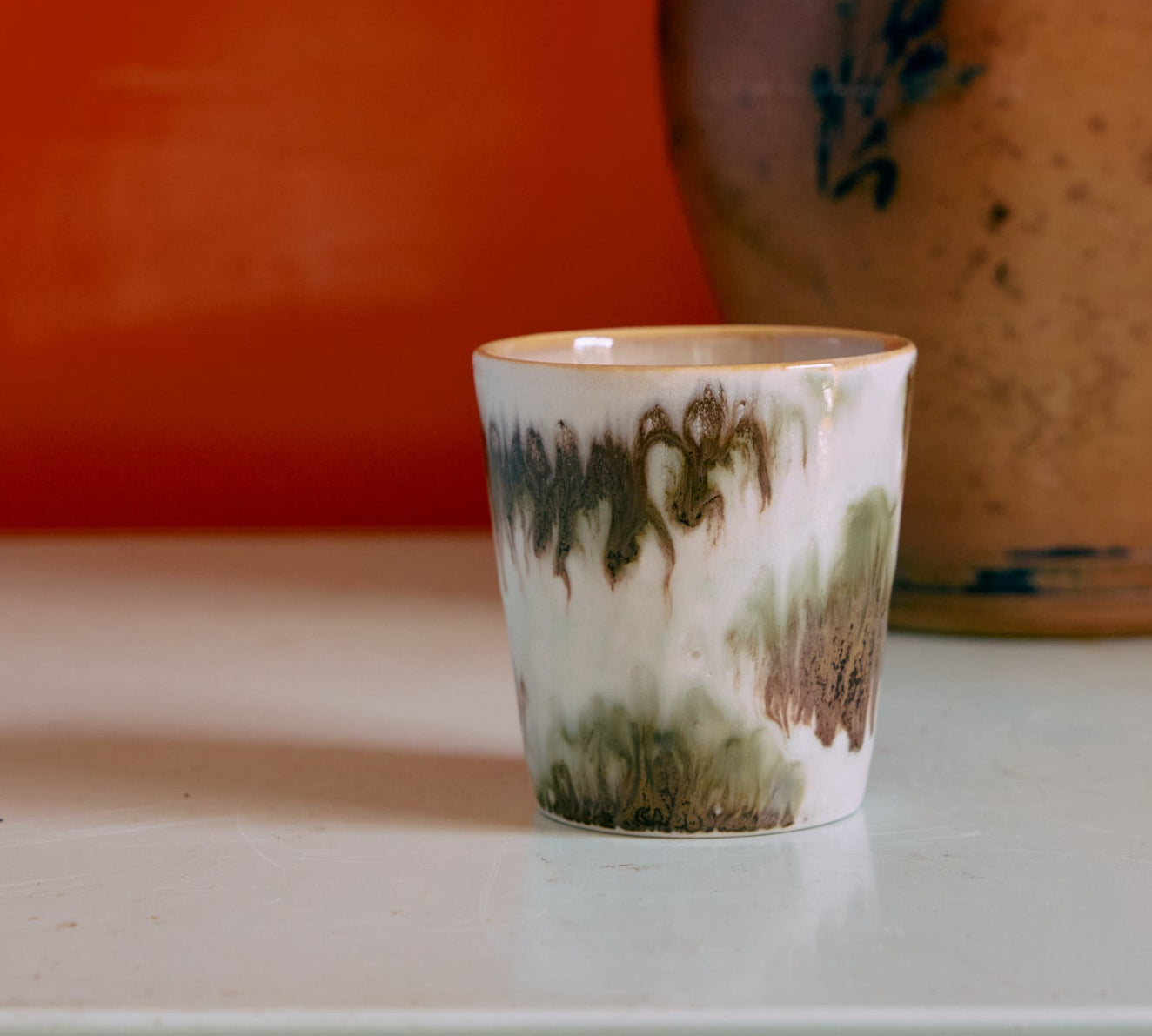 Ceramic cup with abstract green and brown design on a white surface with an orange background