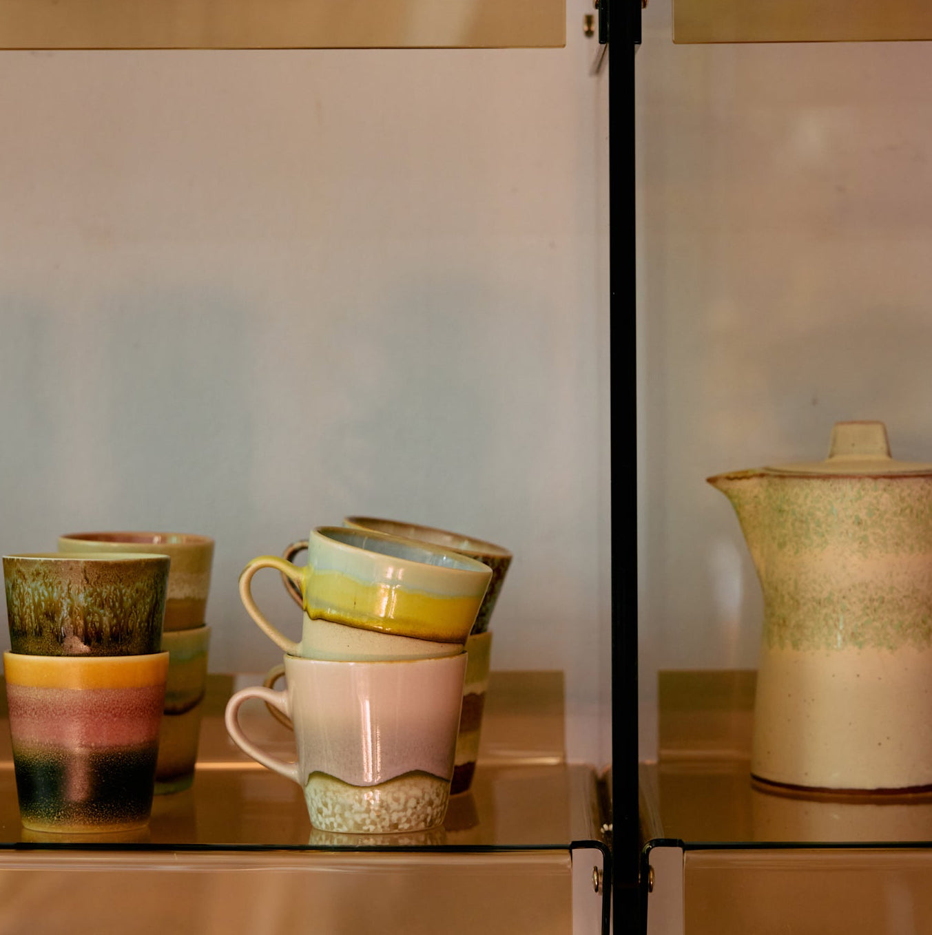 Stack of ceramic mugs with a pitcher on a reflective surface