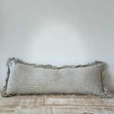 Striped pillow with ruffled edges on a wooden surface against a white wall