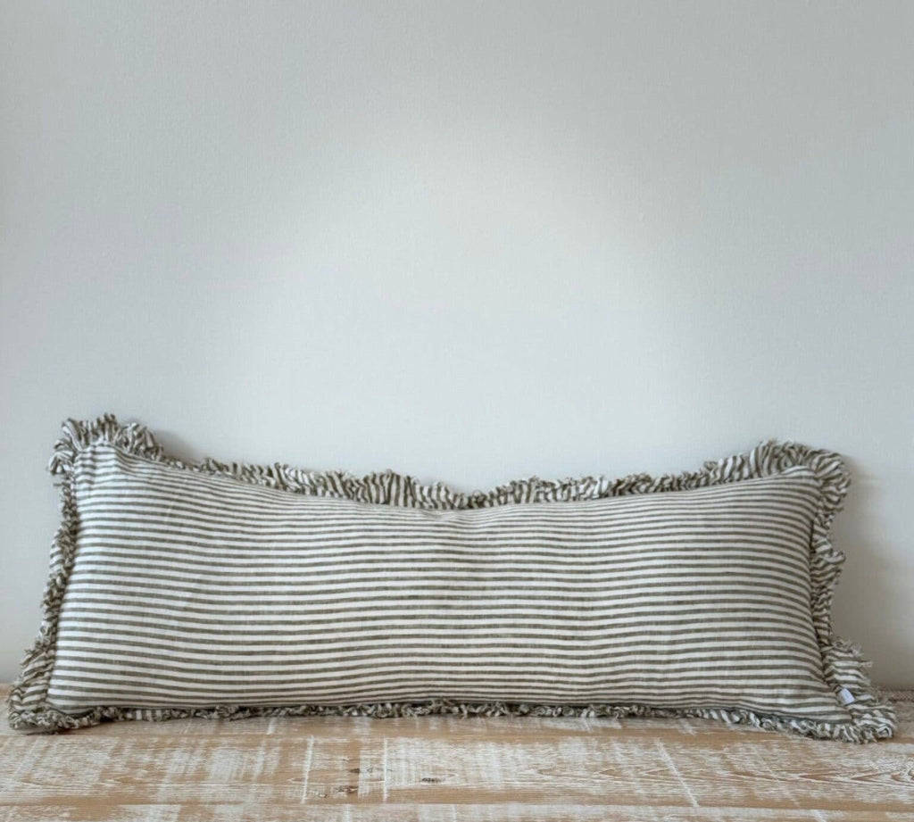Striped pillow with ruffled edges on a wooden surface against a white wall