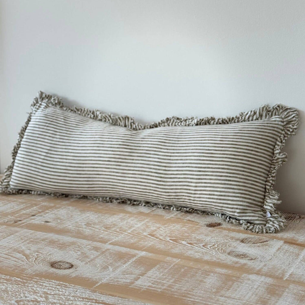 Striped pillow with ruffles on a wooden surface against a white wall