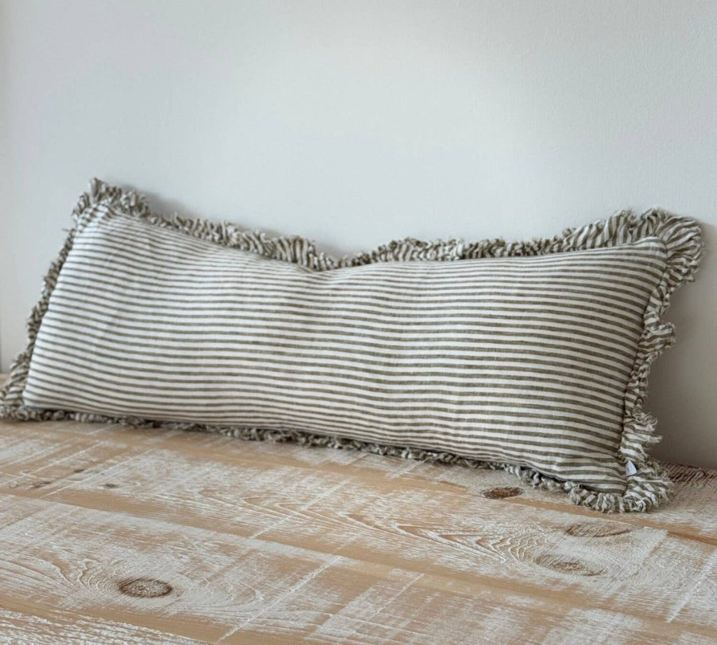 Striped pillow with ruffles on a wooden surface against a white wall