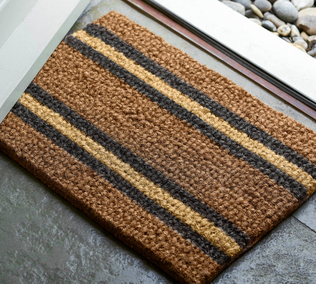 Striped doormat with brown, black, and beige colors on a concrete floor.