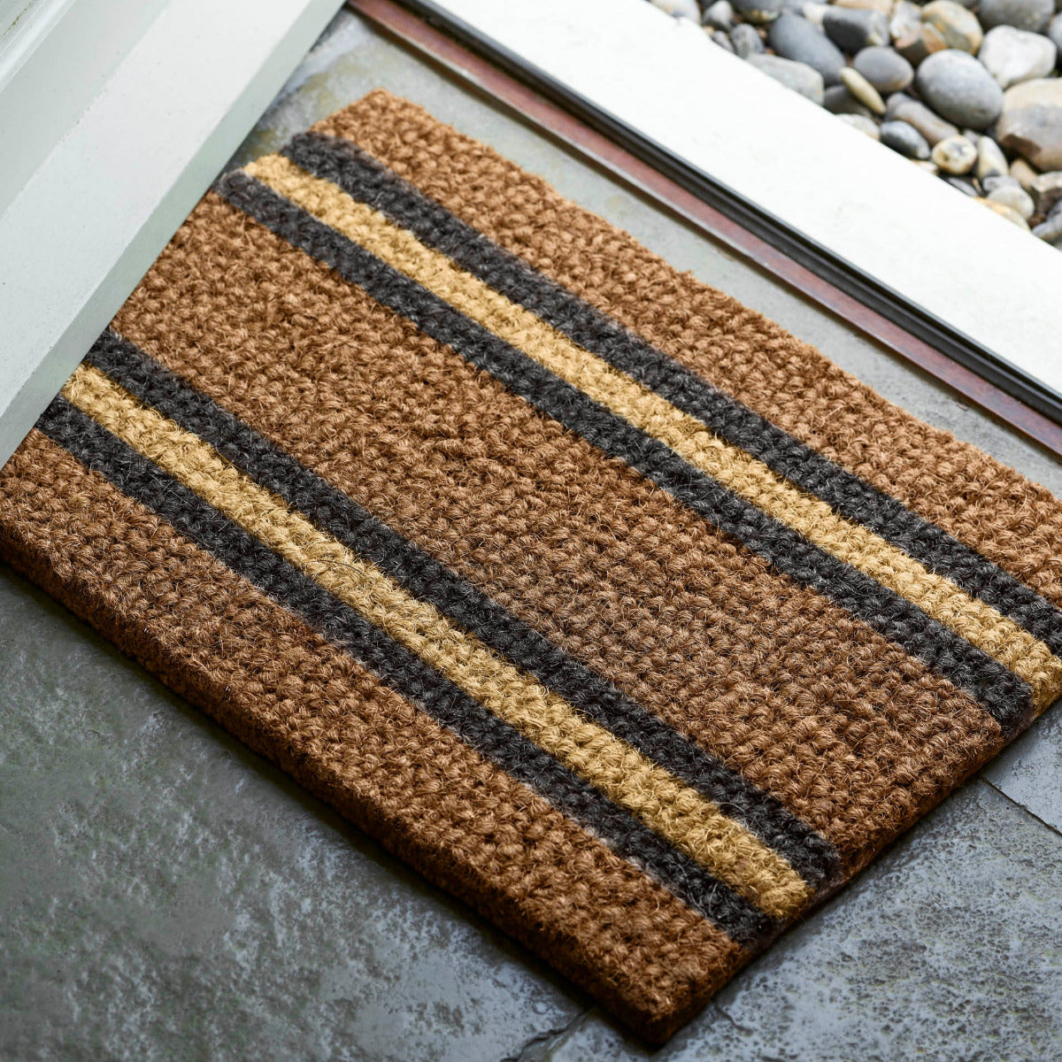 Striped doormat with brown, black, and beige colors on a concrete floor.