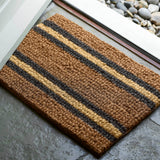 Striped doormat with brown, black, and beige colors on a concrete floor.