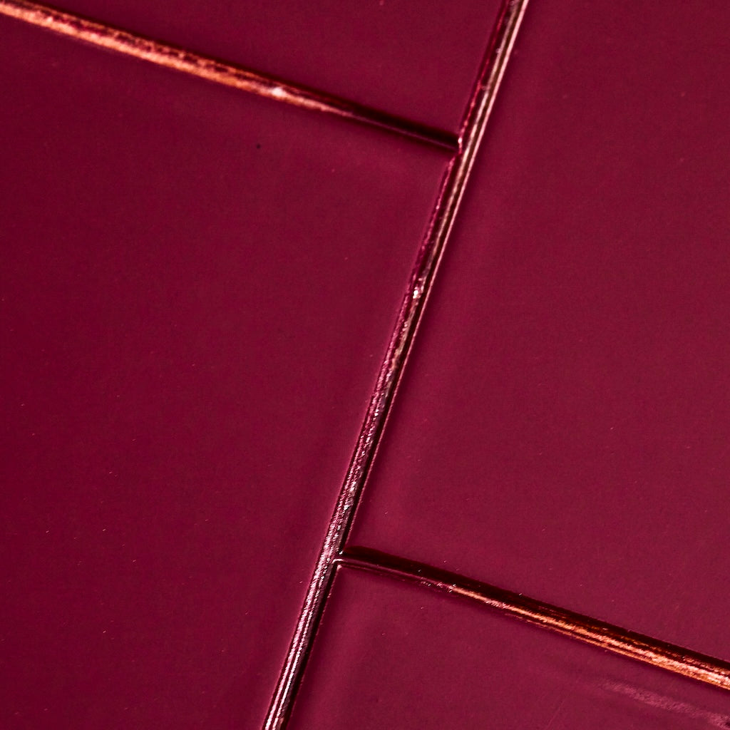 A close-up of glossy rectangular tiles in a deep burgundy or wine color, arranged with metallic copper-toned grout lines.