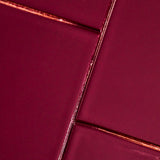 A close-up of glossy rectangular tiles in a deep burgundy or wine color, arranged with metallic copper-toned grout lines.