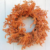 An autumn-themed artificial wreath with dense clusters of orange, rust, and yellow berries on a circular frame, displayed against a white painted wood plank background.