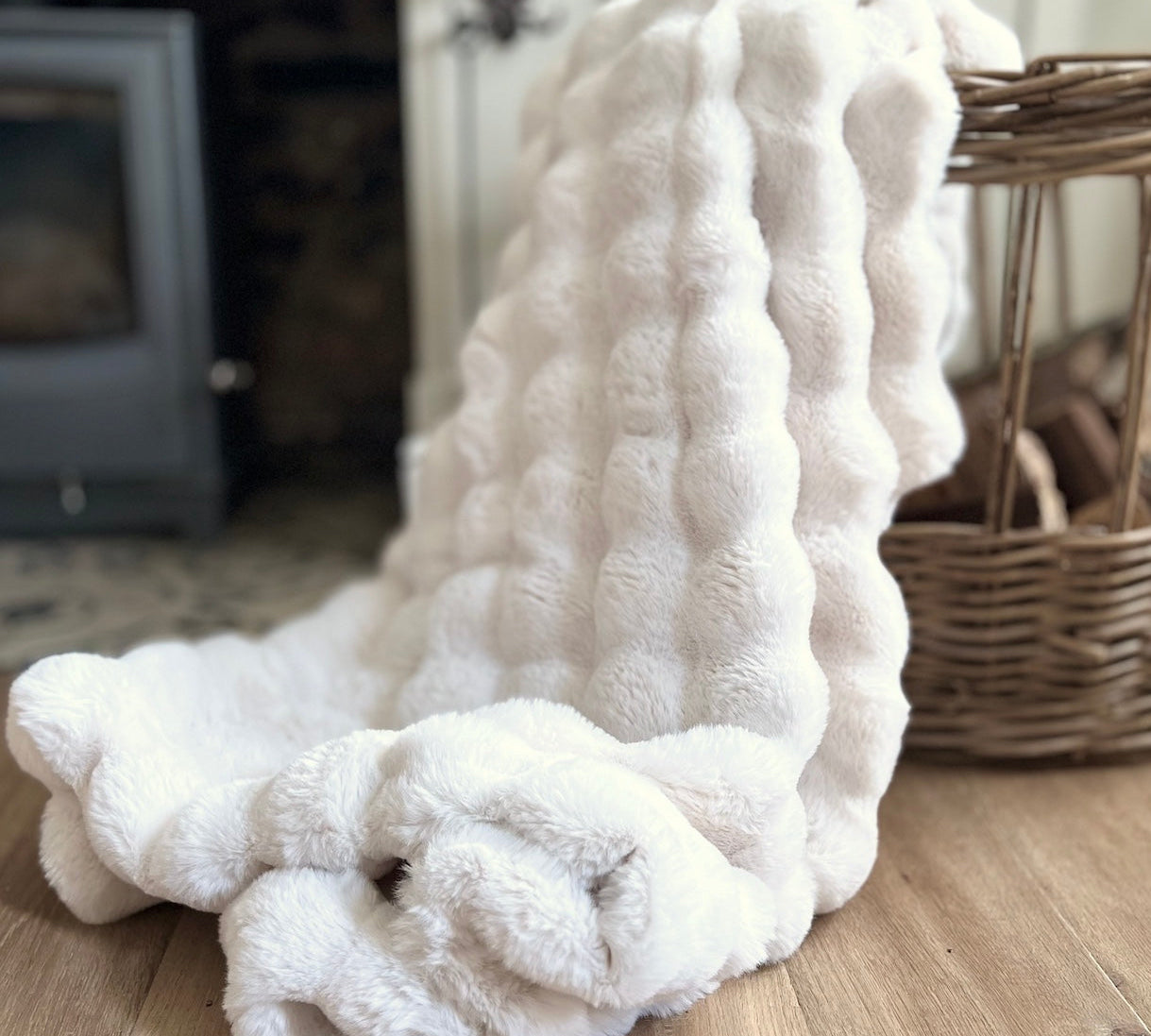 White textured blanket on a wooden floor with a wicker basket in the background