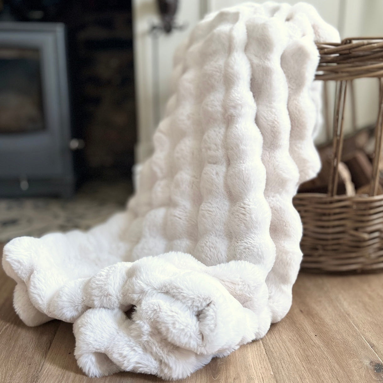 White textured blanket on a wooden floor with a wicker basket in the background