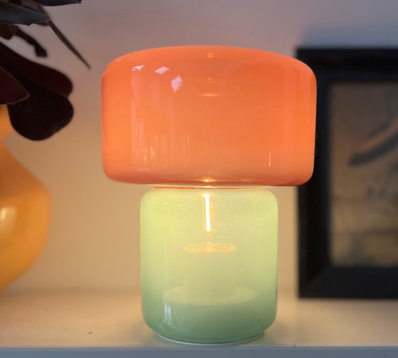 Decorative lamp with a pink top and green base on a shelf.