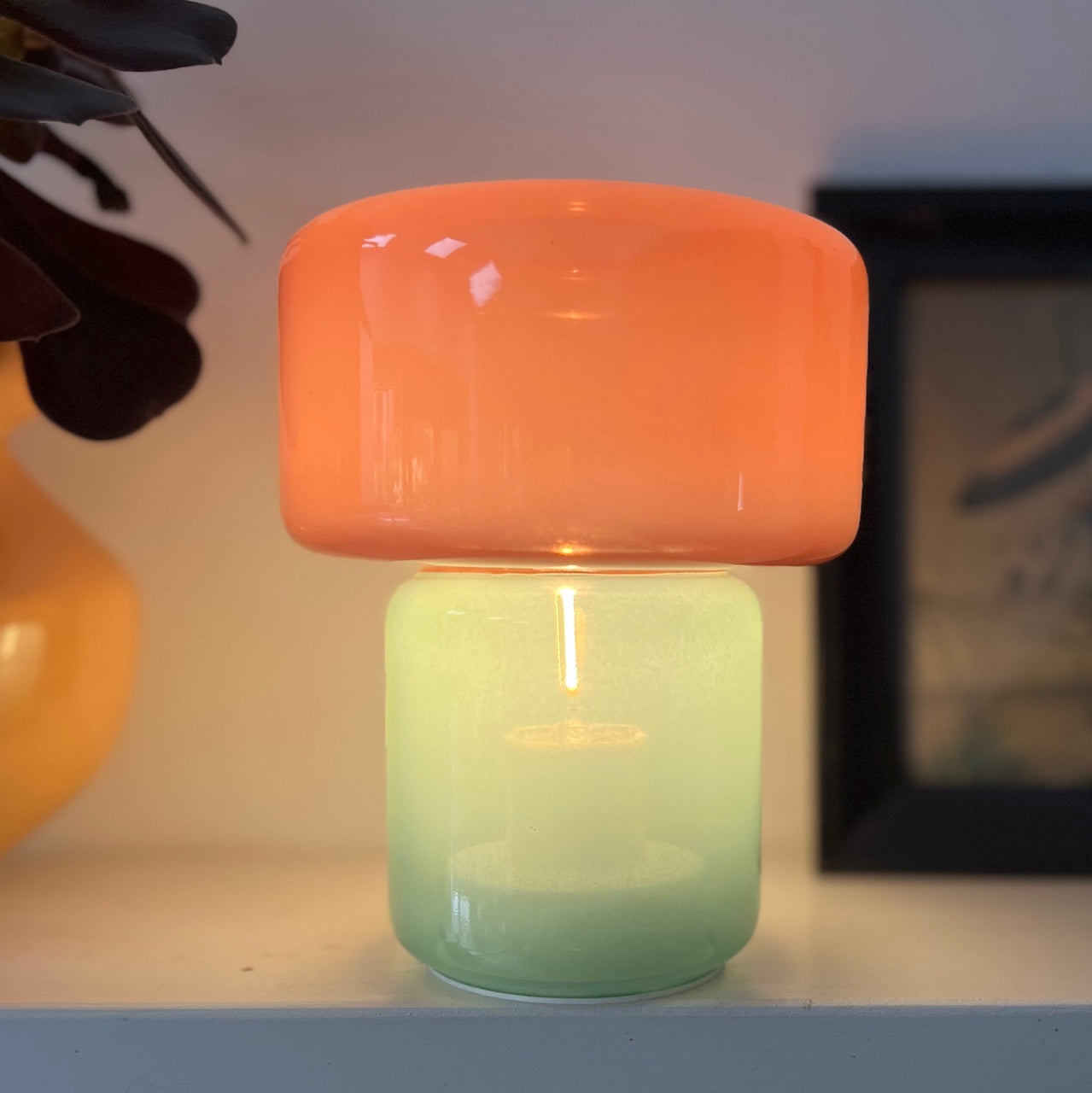 Decorative lamp with a pink top and green base on a shelf.